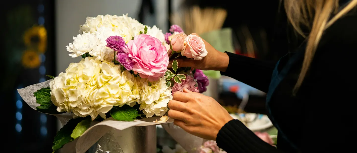 A florist finishing a bouquet of hydrangeas and roses for a customer order