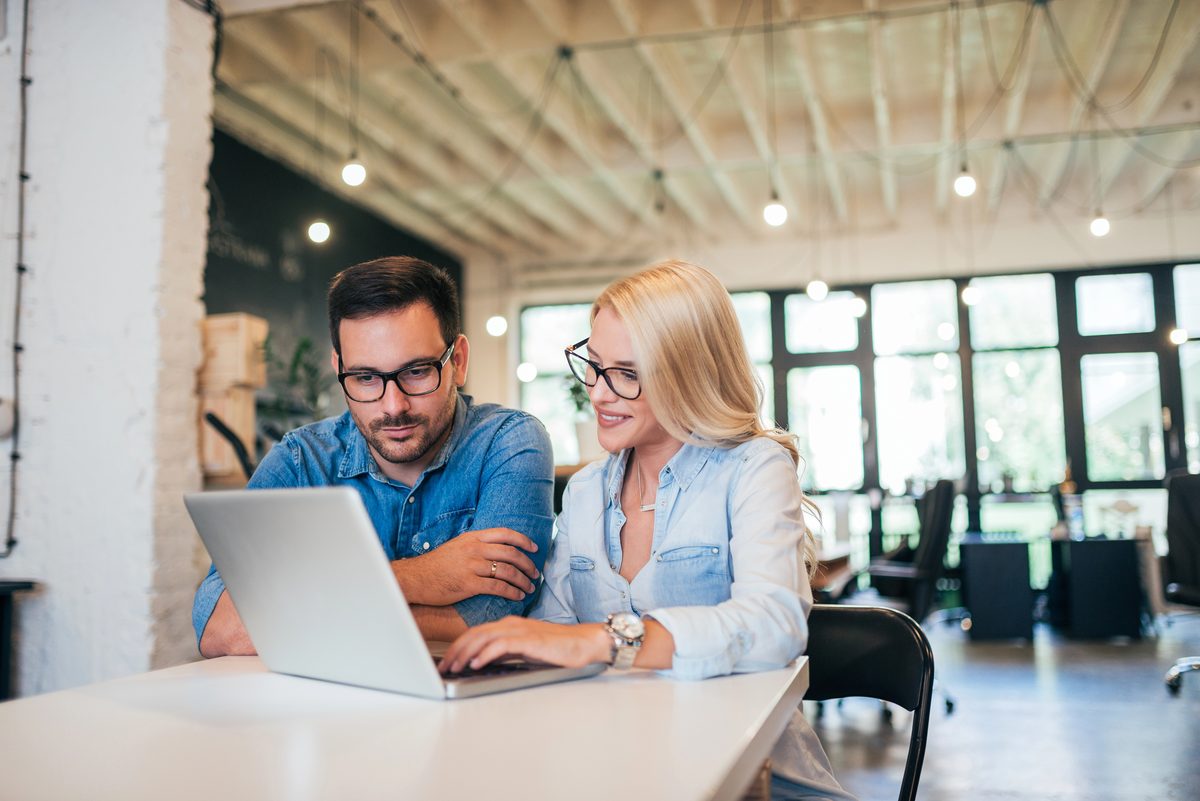 Two business owners reviewing a website together on a laptop in a bright, open office