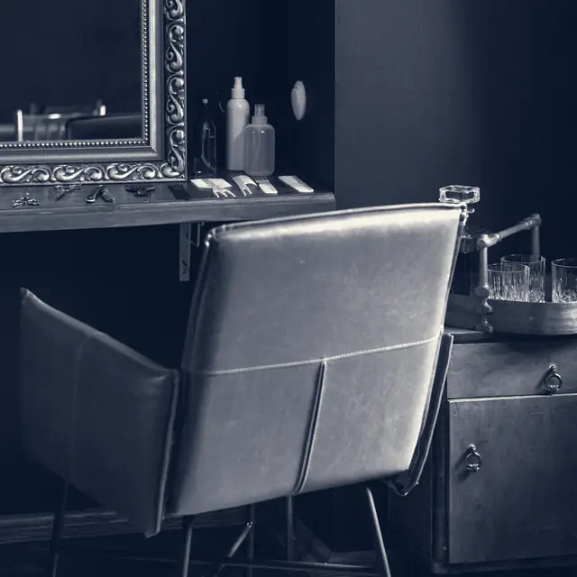 A leather styling chair before a gilt mirror on a dark wall