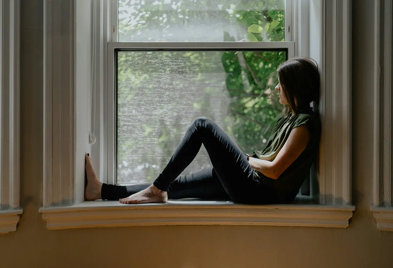 A woman sitting peacefully on a window seat in soft daylight